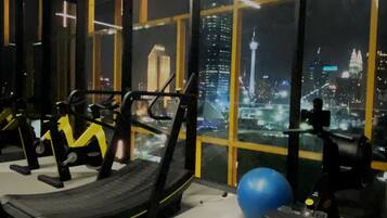 A gym with exercise equipment and a large window overlooking a cityscape at night.