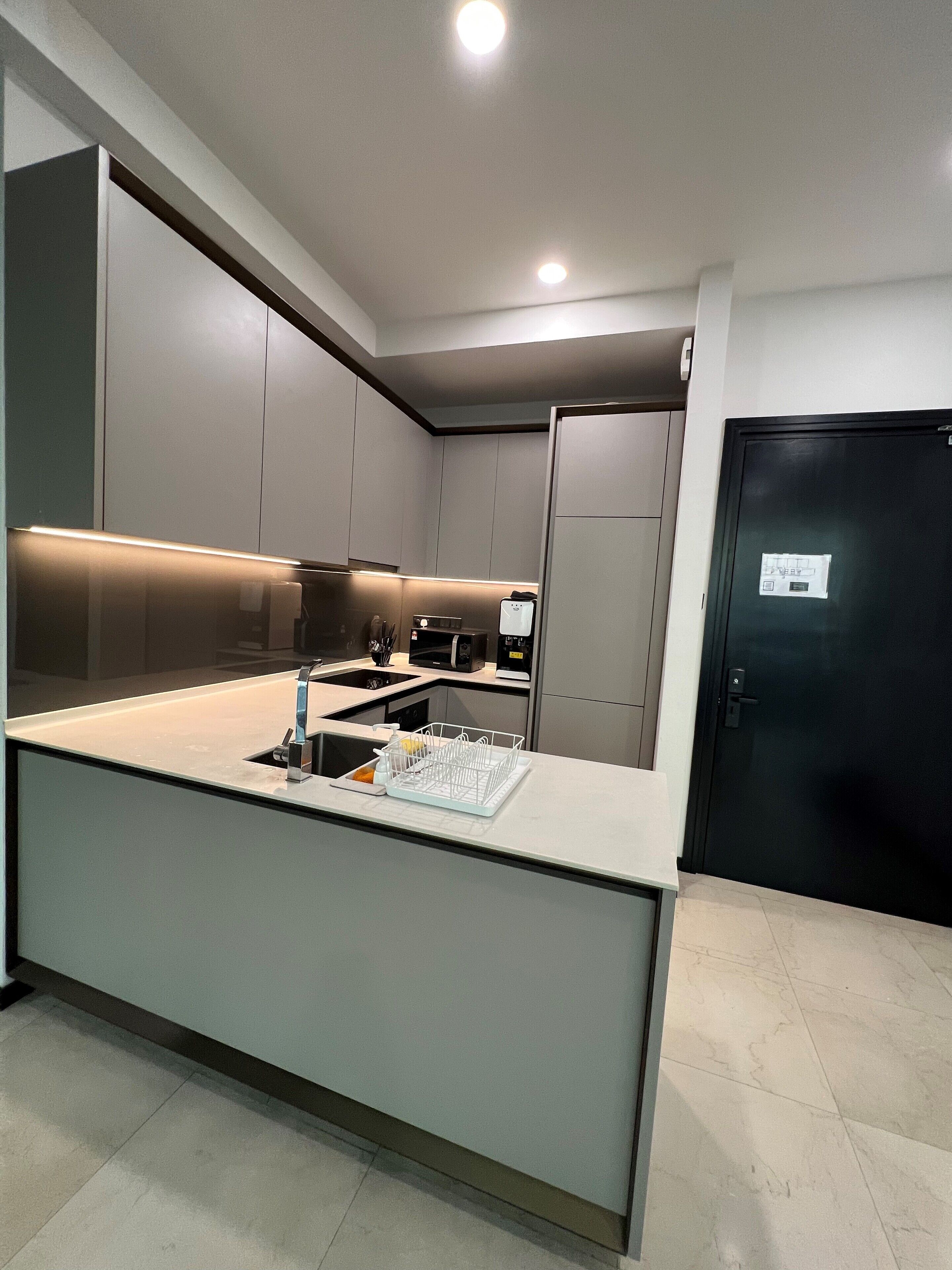 A modern kitchen with a central island, built-in appliances, and a black door.