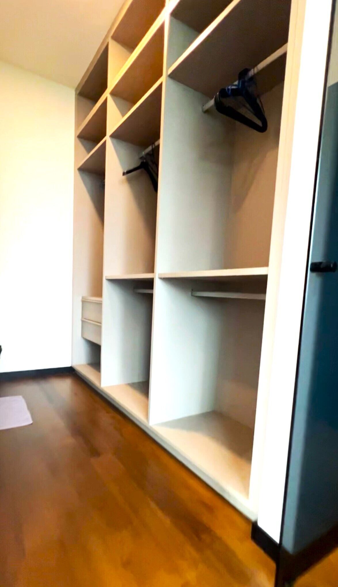 A walk-in closet with multiple shelves and hanging space, a wooden floor, and a white door.