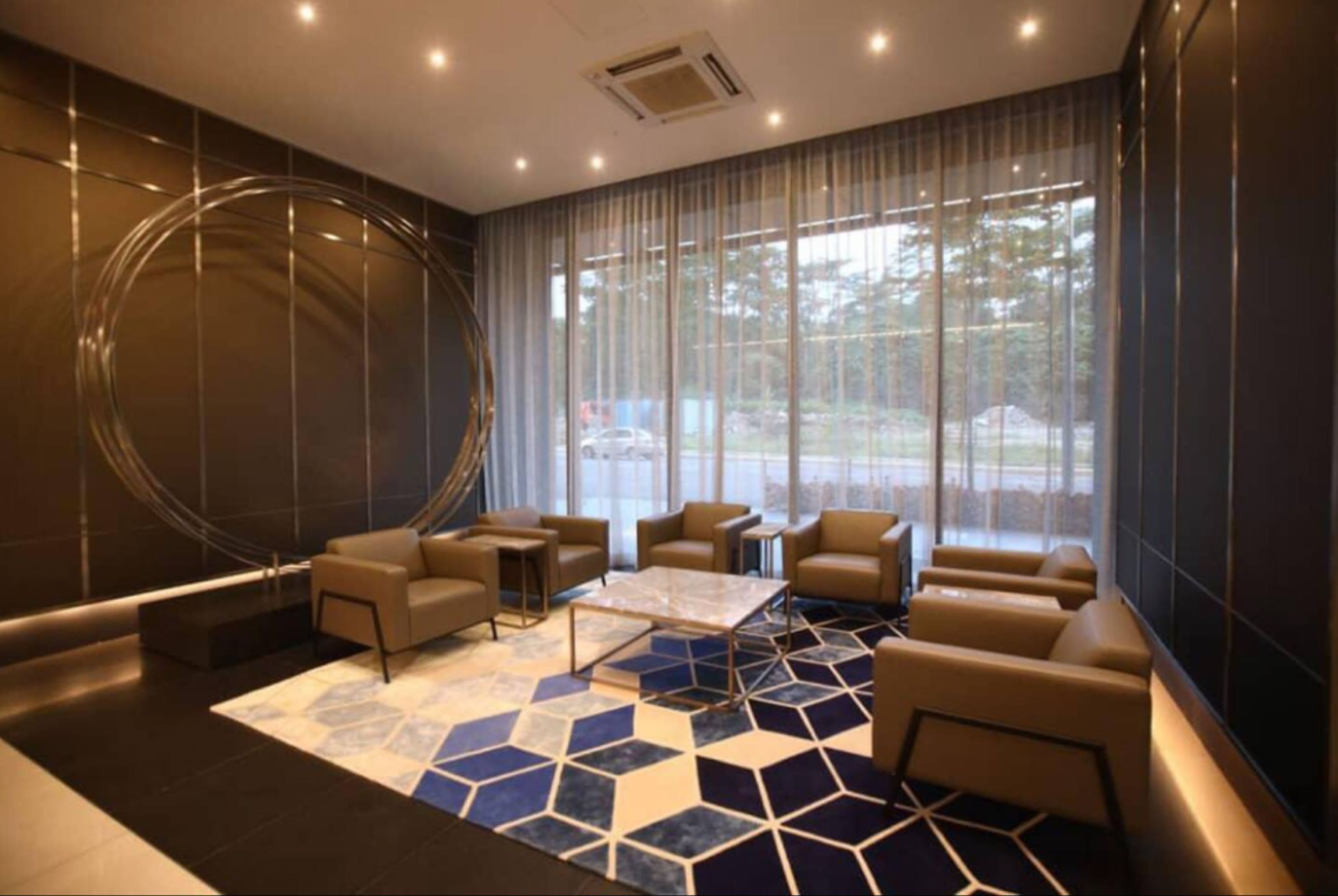 Un moderno hall de hotel con alfombra de diseño geométrico, asientos de cuero, una mesa de centro y grandes ventanales con cortinas translúcidas.