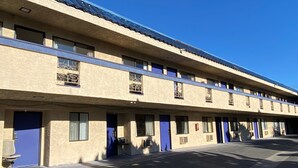 A motel with a row of rooms, each with a blue door and a window with a decorative grille. - Star Inn Motel (Costa Mesa)