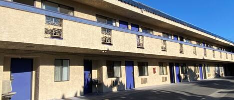 A motel with a row of rooms, each with a blue door and a window with a decorative grille.