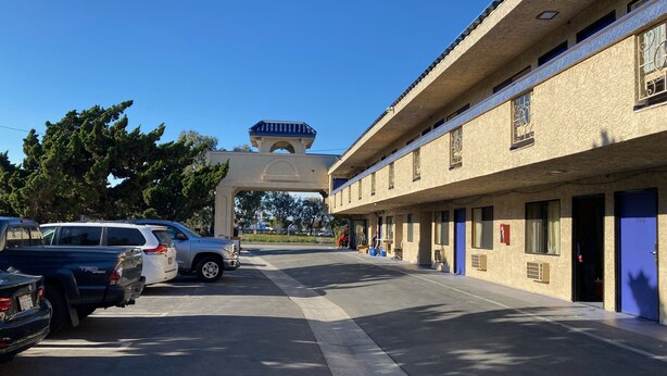A motel with a row of rooms, a covered entrance, and parked cars. - Star Inn Motel (Costa Mesa)