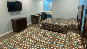 A hotel room with two beds, a desk, a chair, a television, and a bathroom visible in the background. - Star Inn Motel (Costa Mesa)