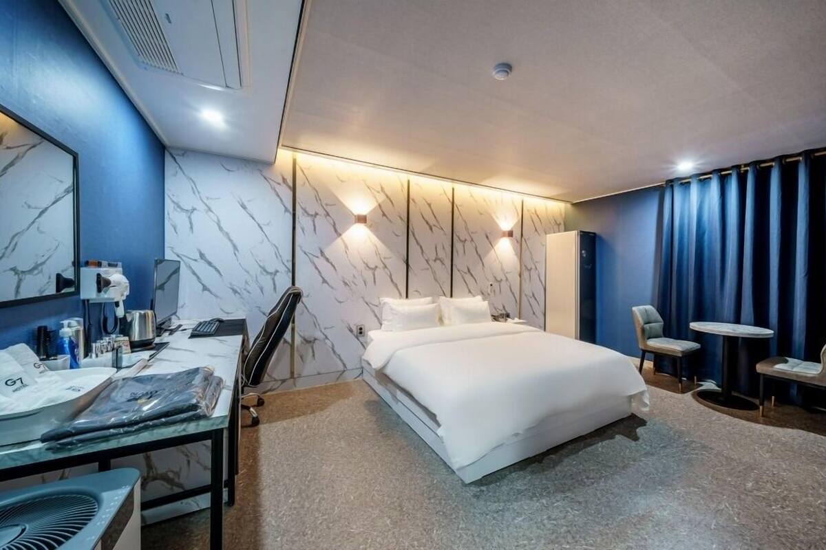 A modern hotel room with a large bed, a desk with a chair, a small table, and a mirror.