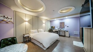 Una habitación de hotel moderna con una cama grande, un escritorio con ordenador, una silla y una mesita.