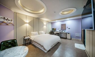 A modern hotel room with a large bed, a desk with a computer, a chair, and a small table.