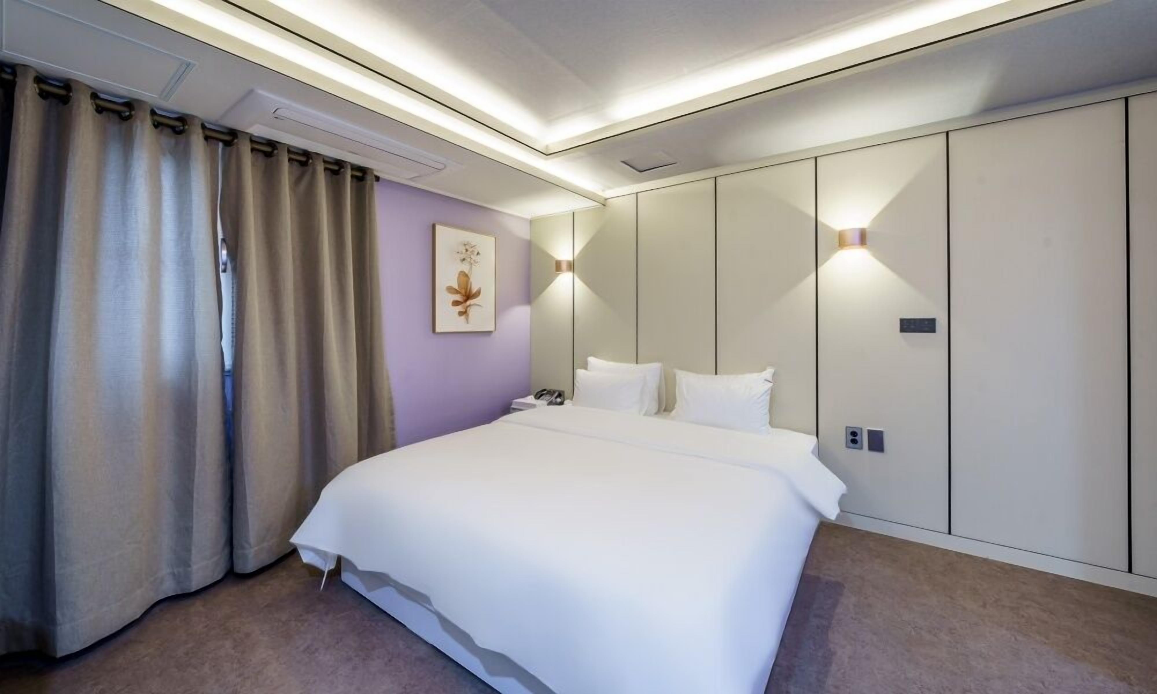 Een moderne hotelkamer met een groot bed, beige gordijnen, een wandlamp en een ingelijste foto.