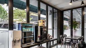 Un café moderno con una máquina de café, un dispensador de bebidas y un área de estar con mesas y sillas.