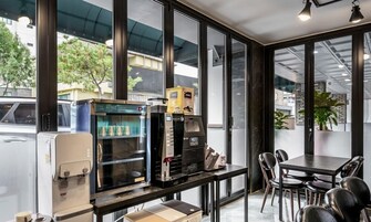 A modern cafe interior with a coffee machine, a beverage dispenser, and a seating area with tables and chairs.