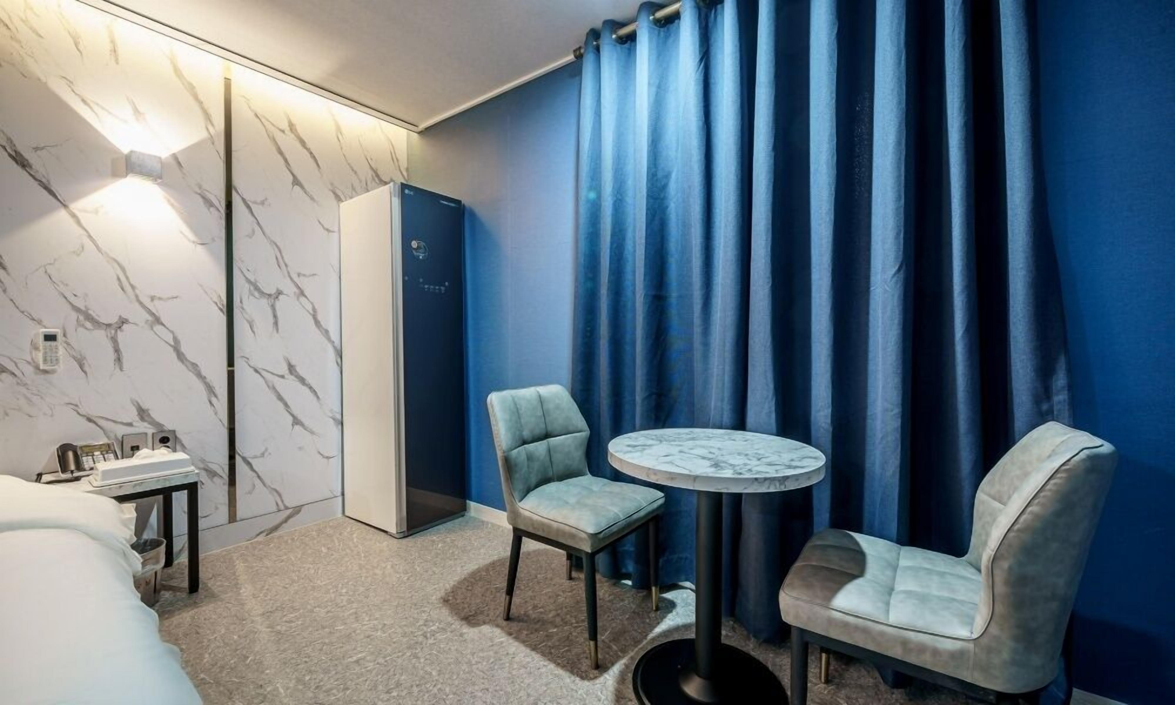 Hotelkamer met een wand met marmerlook, een bed, een bureau met telefoon, twee stoelen, een klein rond tafeltje en een kledingkast.