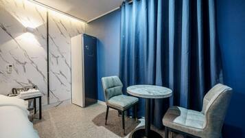 A hotel room with a marble-patterned wall, a bed, a desk with a telephone, two chairs, a small round table, and a wardrobe.