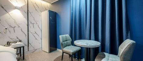 Hotelkamer met een wand met marmerlook, een bed, een bureau met telefoon, twee stoelen, een klein rond tafeltje en een kledingkast.