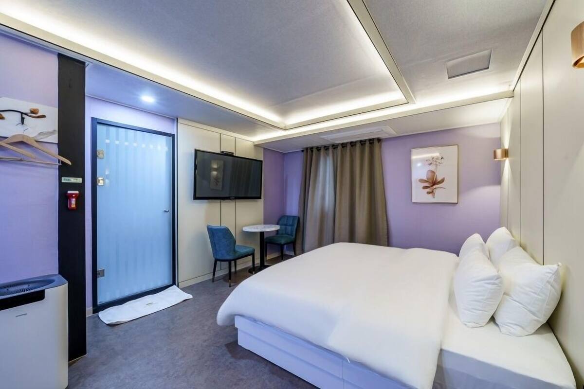 A hotel room with a bed, a desk, a chair, a TV, and a bathroom.