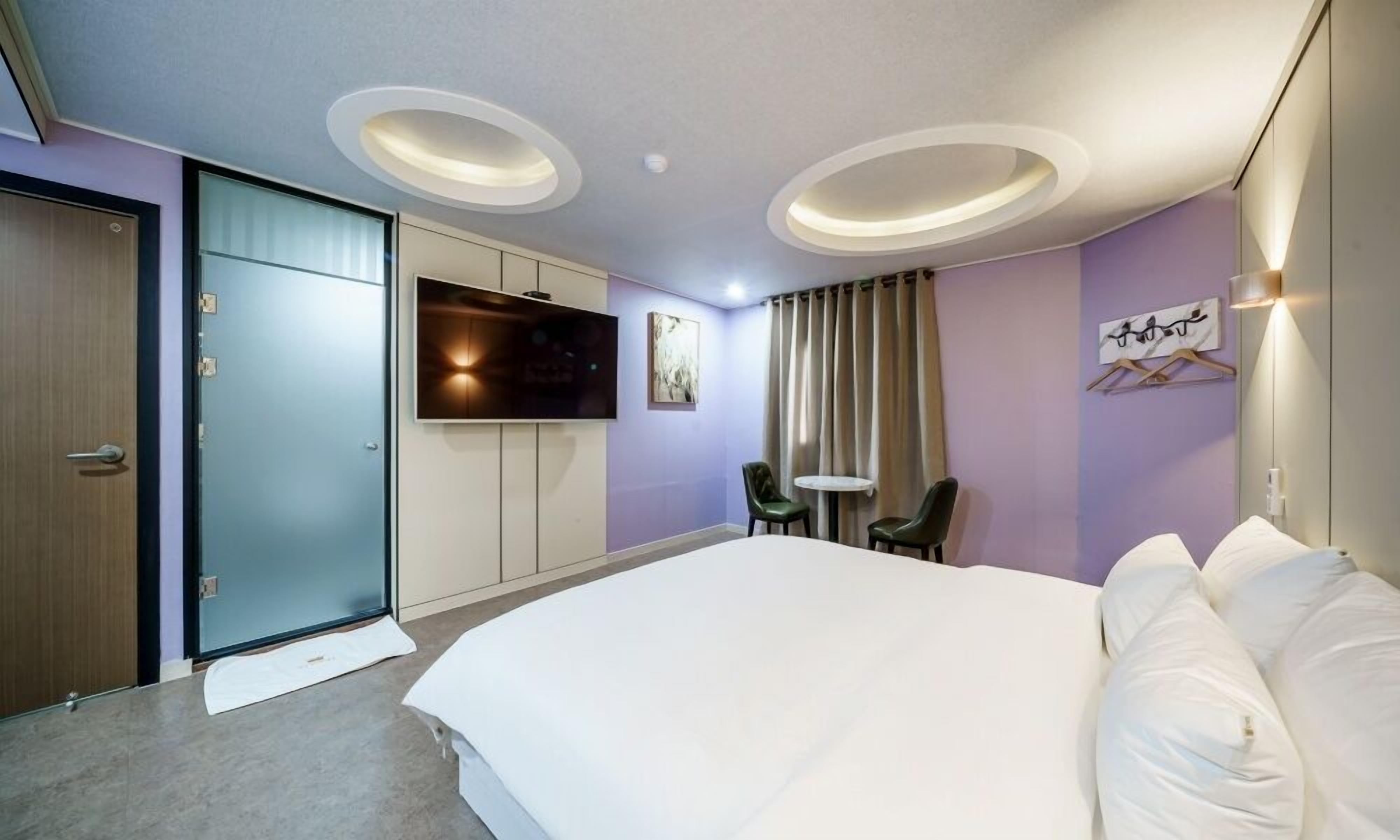 A hotel room with a large bed, a flat-screen TV, a small table, two chairs, and a sliding door.