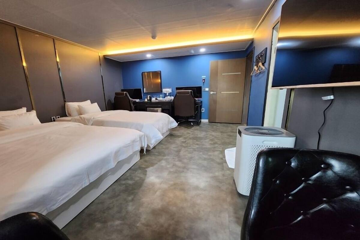 A hotel room with two beds, a desk, a chair, and a wardrobe.