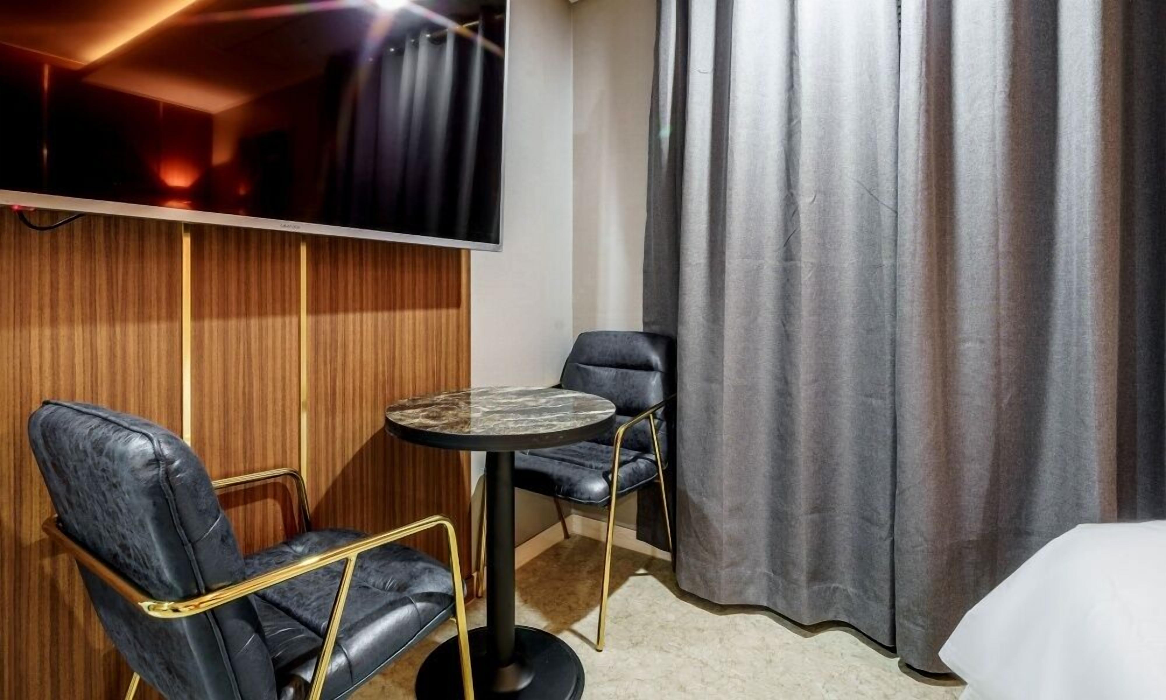 A hotel room with a round table, two chairs, a bed, a TV mounted on the wall, and a curtain.