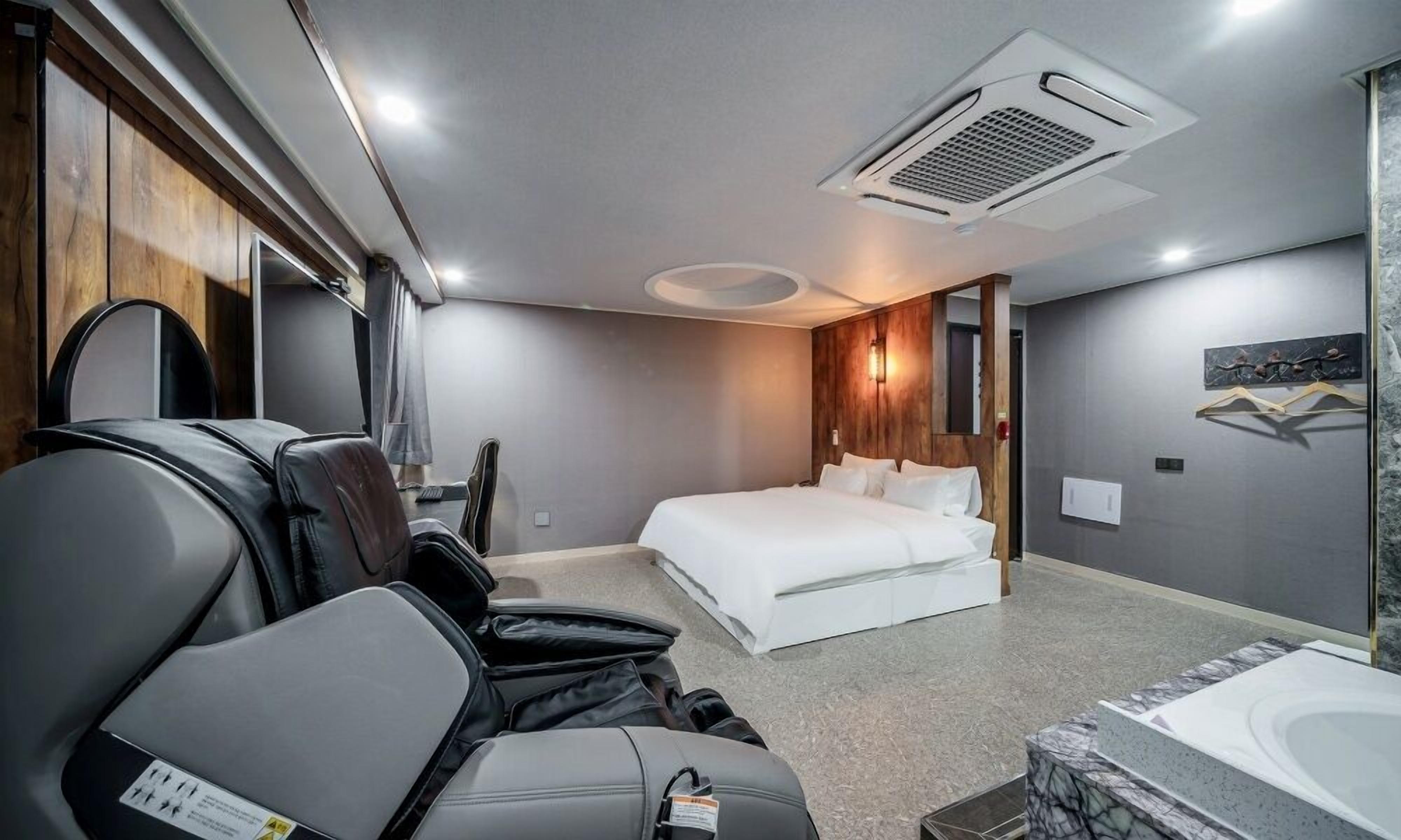 A modern hotel room with a bed, a massage chair, a small desk, and a shower area.
