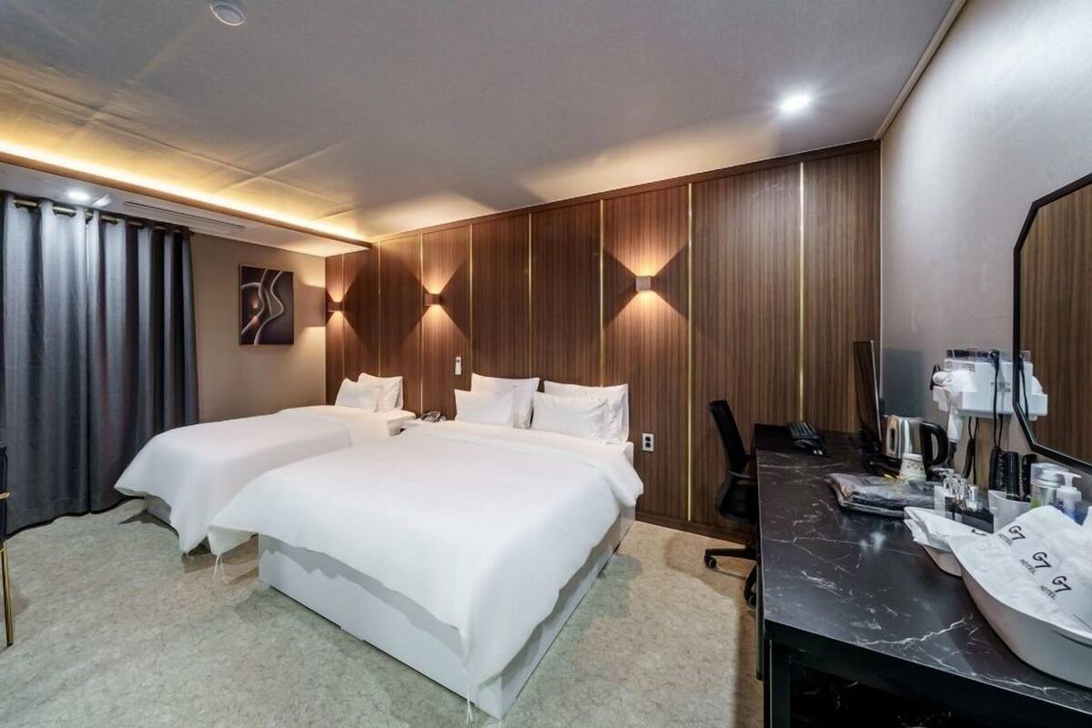 A hotel room with two beds, a desk, and a mirror.