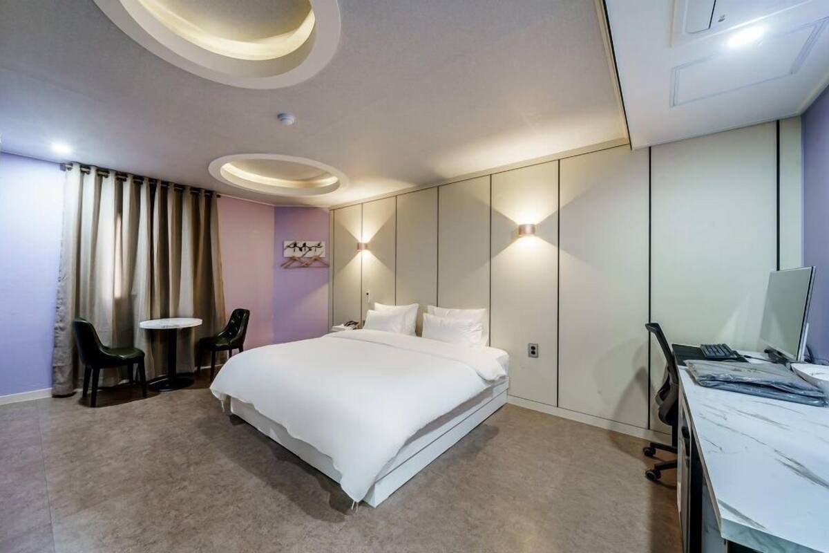 A modern hotel room with a large bed, a desk with a computer, and a seating area with two chairs.