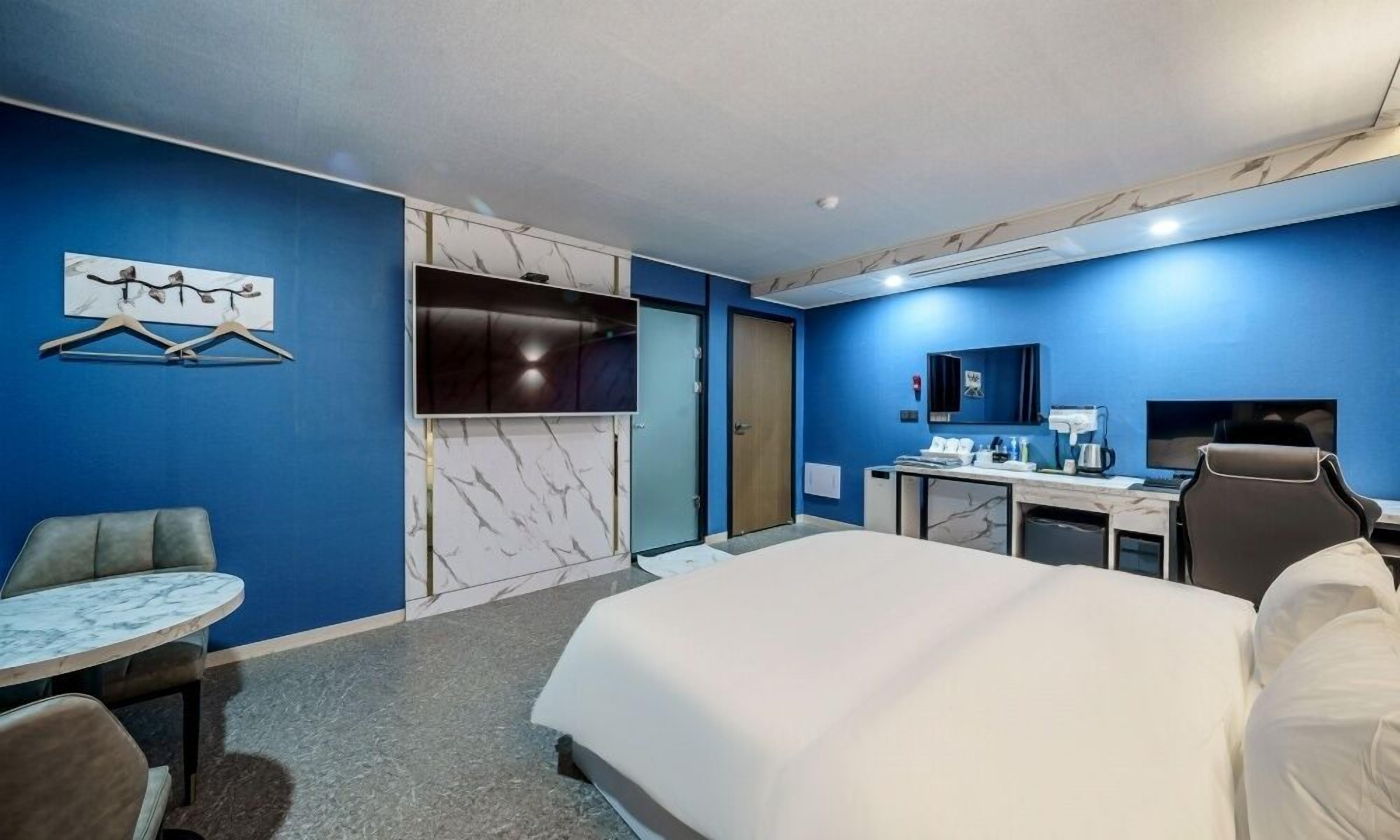 Quarto de hotel com uma cama, escrivaninha, cadeira, televisão e guarda-roupa.