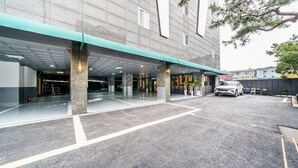 Un edificio moderno con entrada cubierta, zona de estacionamiento y un coche blanco aparcado fuera.