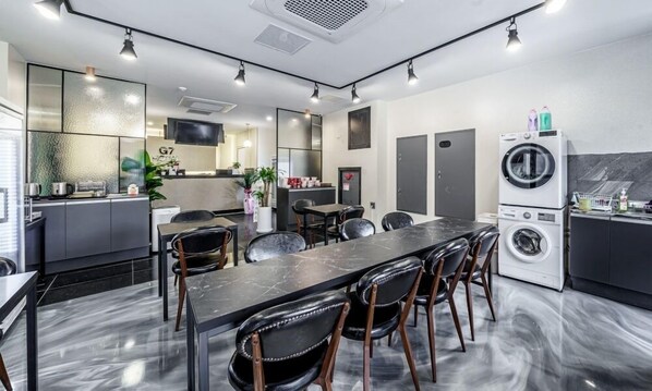 Una habitación de hotel moderna con una mesa de comedor de mármol, sillas de cuero negro, un área de cocina con lavadora y un televisor montado en la pared.