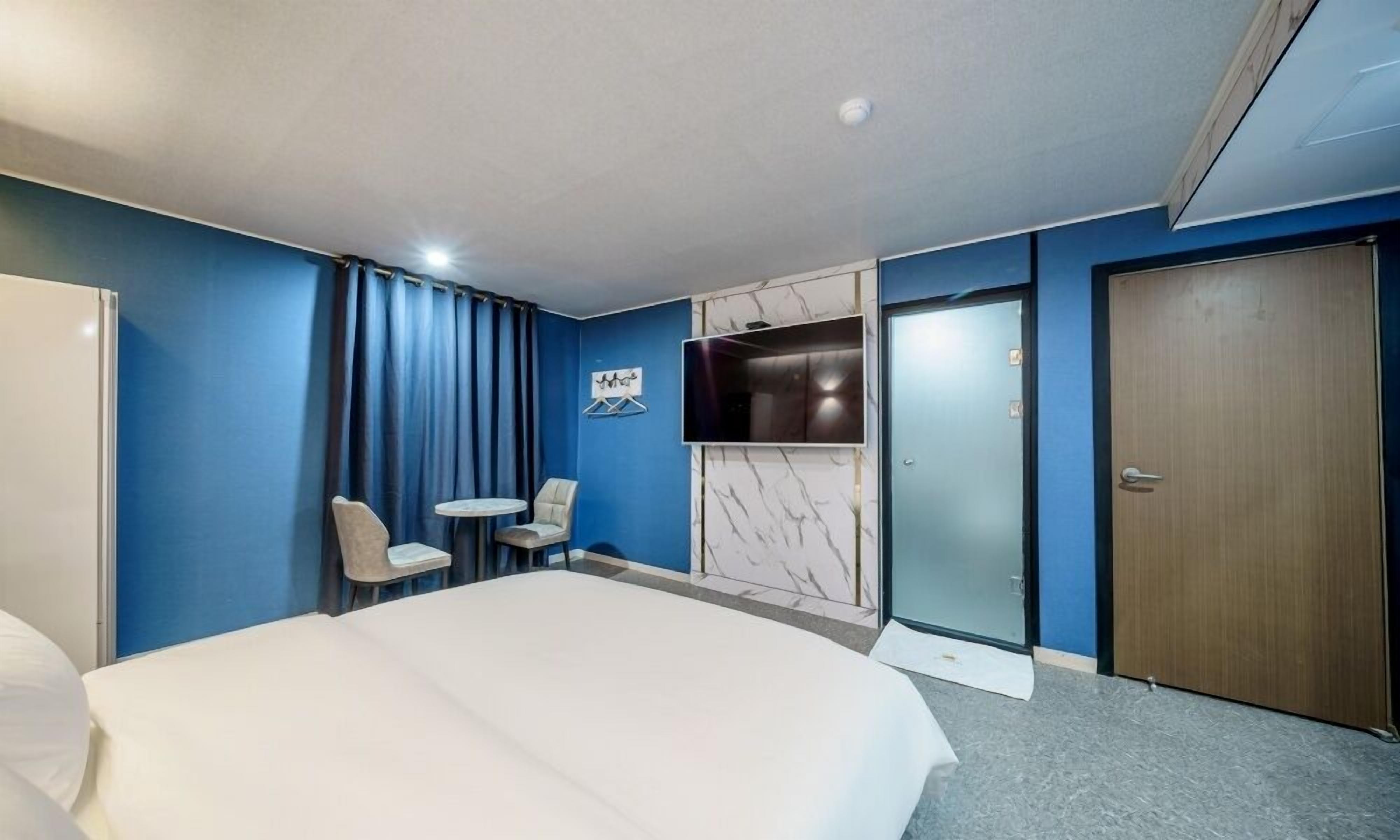A hotel room with a large bed, two chairs, a TV, and a door.