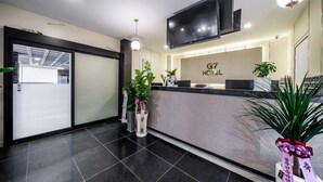 Zona de recepción de un hotel con diseño moderno, que incluye un mostrador de recepción, un televisor de pantalla plana y un letrero que dice "G7 Hotel".