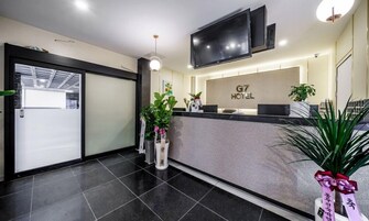 A hotel reception area with a modern design, including a reception desk, a flat-screen TV, and a sign that reads "G7 Hotel".