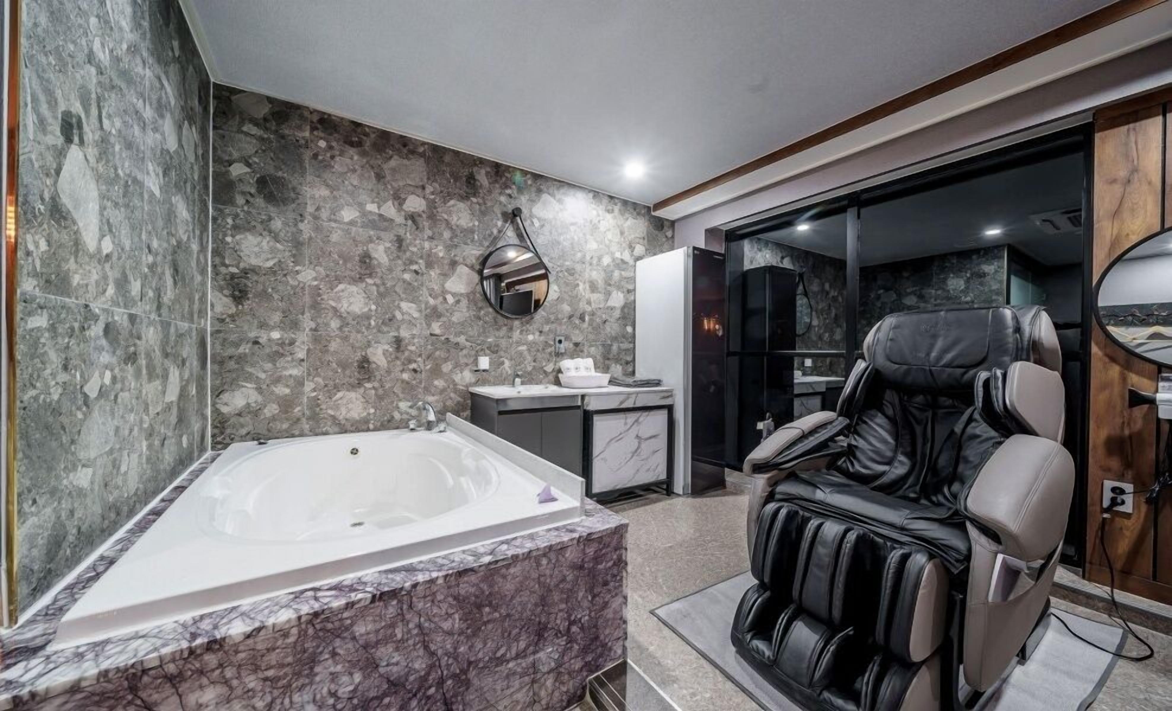 Un baño moderno con una bañera grande, una silla de masajes y un tocador con encimera de mármol.