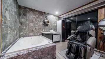 Un baño moderno con una bañera grande, una silla de masajes y un tocador con encimera de mármol.