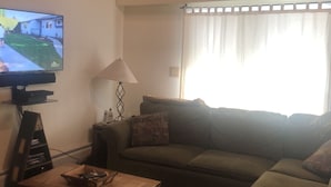Sala de estar com televisão, sofá, mesa de centro e janela com cortinas.