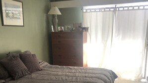 Quarto com uma cama grande, cômoda, luminária e janela com cortinas.