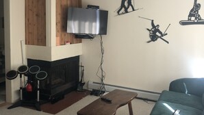 Sala de estar com lareira, televisão e obras de arte que retratam atividades ao ar livre.