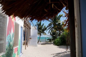 Un sendero frente al mar que conduce a un edificio con techo de paja, rodeado de palmeras y una playa de arena.