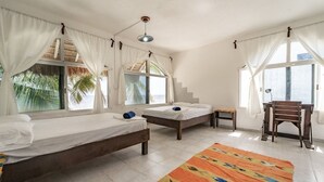 Quarto com duas camas, uma mesa pequena, uma cadeira e uma janela grande com cortinas.