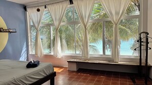 A room with a bed, a bench, and large windows with curtains. - Pronoia Casa de Playa (Mahahual)