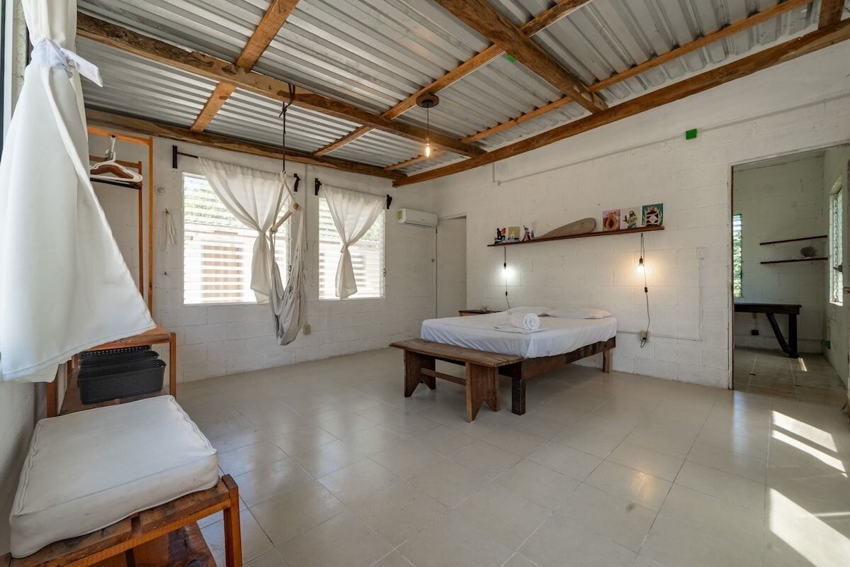 A bedroom with a bed, a bench, a hanging chair, and a window with curtains.