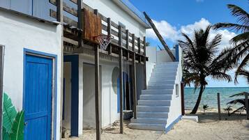 Una casa de playa con una puerta azul, una escalera que lleva a una terraza de madera y vistas al océano.