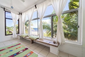 Una habitación con ventanas amplias, un banco con cojines y una alfombra colorida.