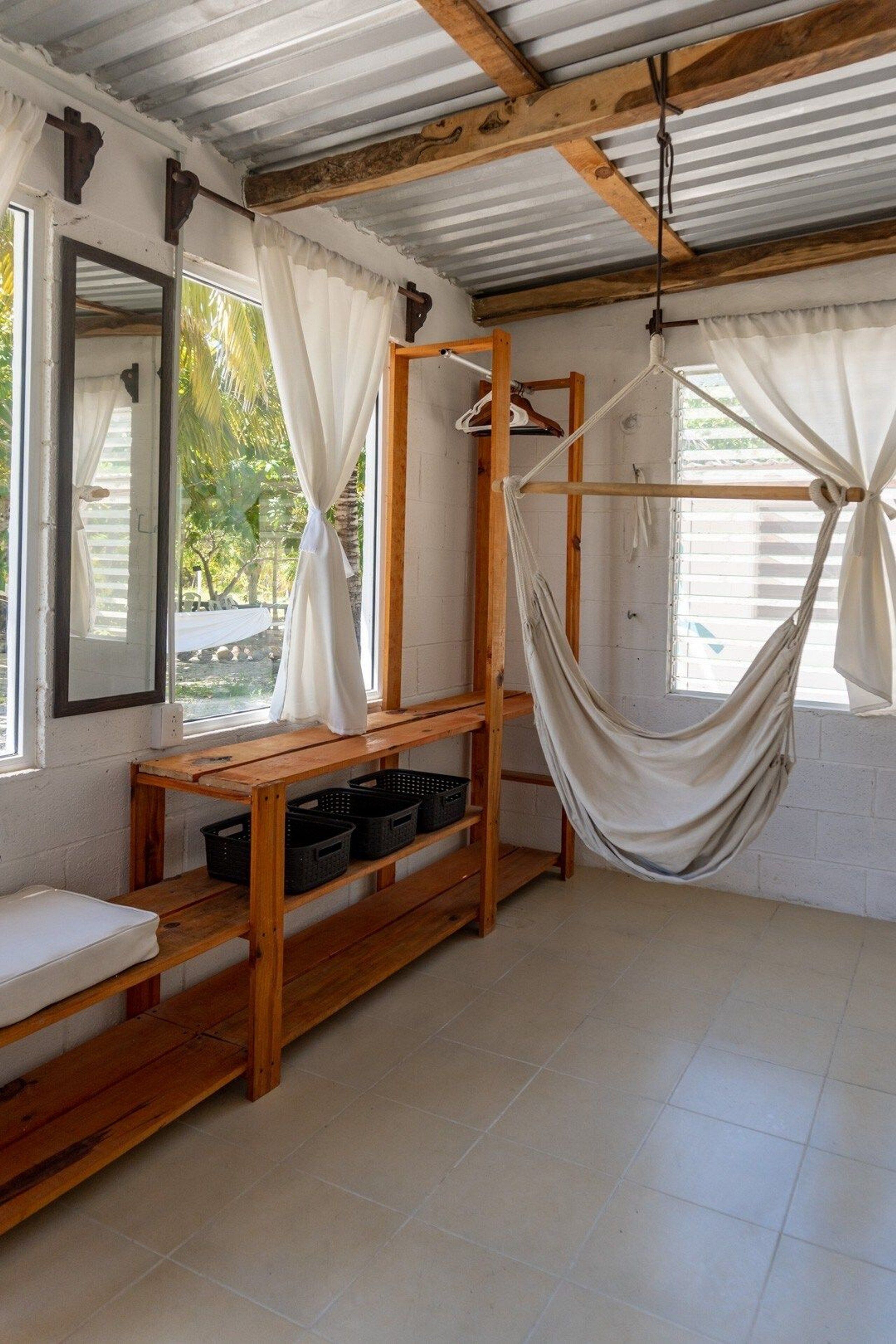 Una habitación con una hamaca, estanterías de madera, un colchón y un espejo.