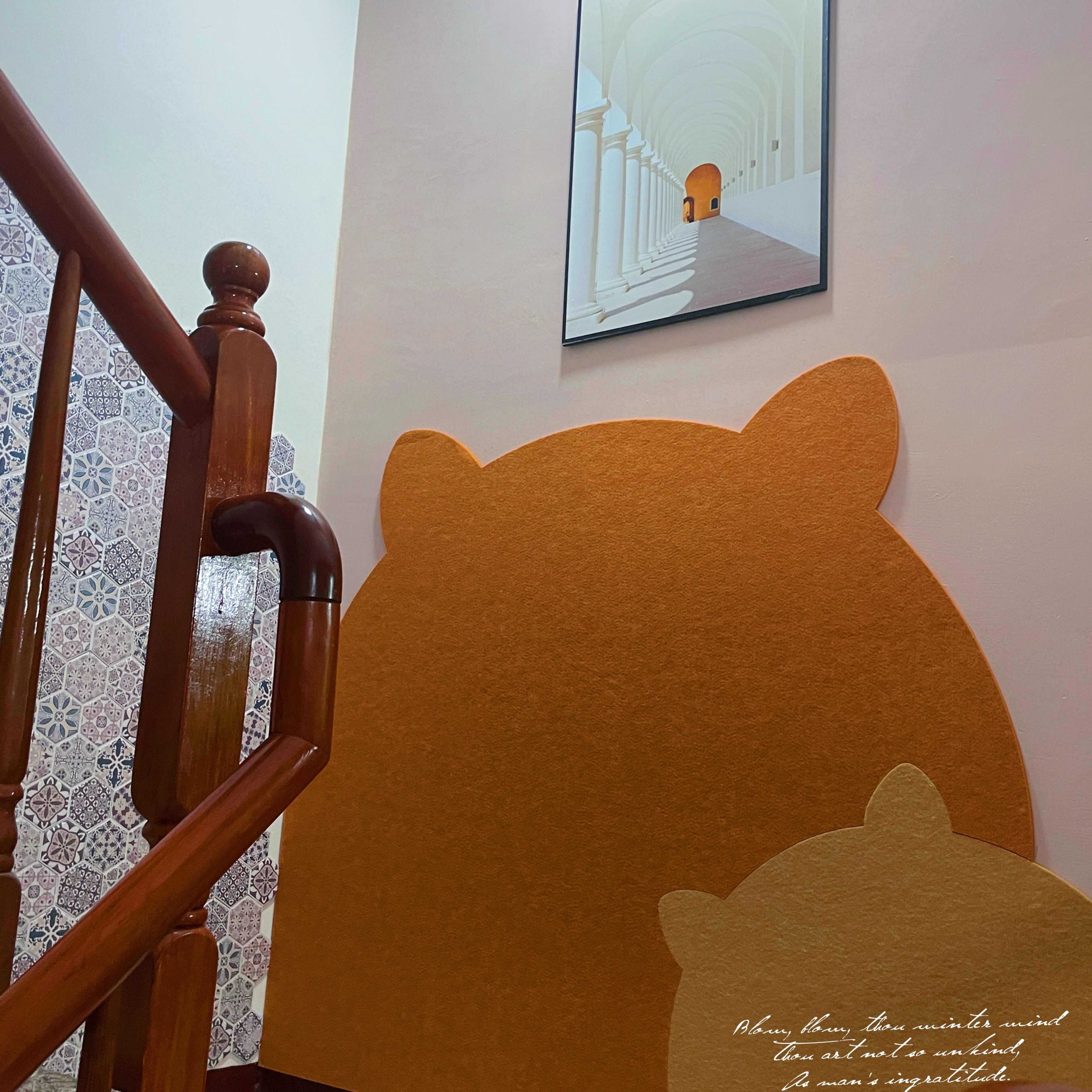 A staircase with a wooden handrail and a wall with a large bear cutout and a framed picture above it.