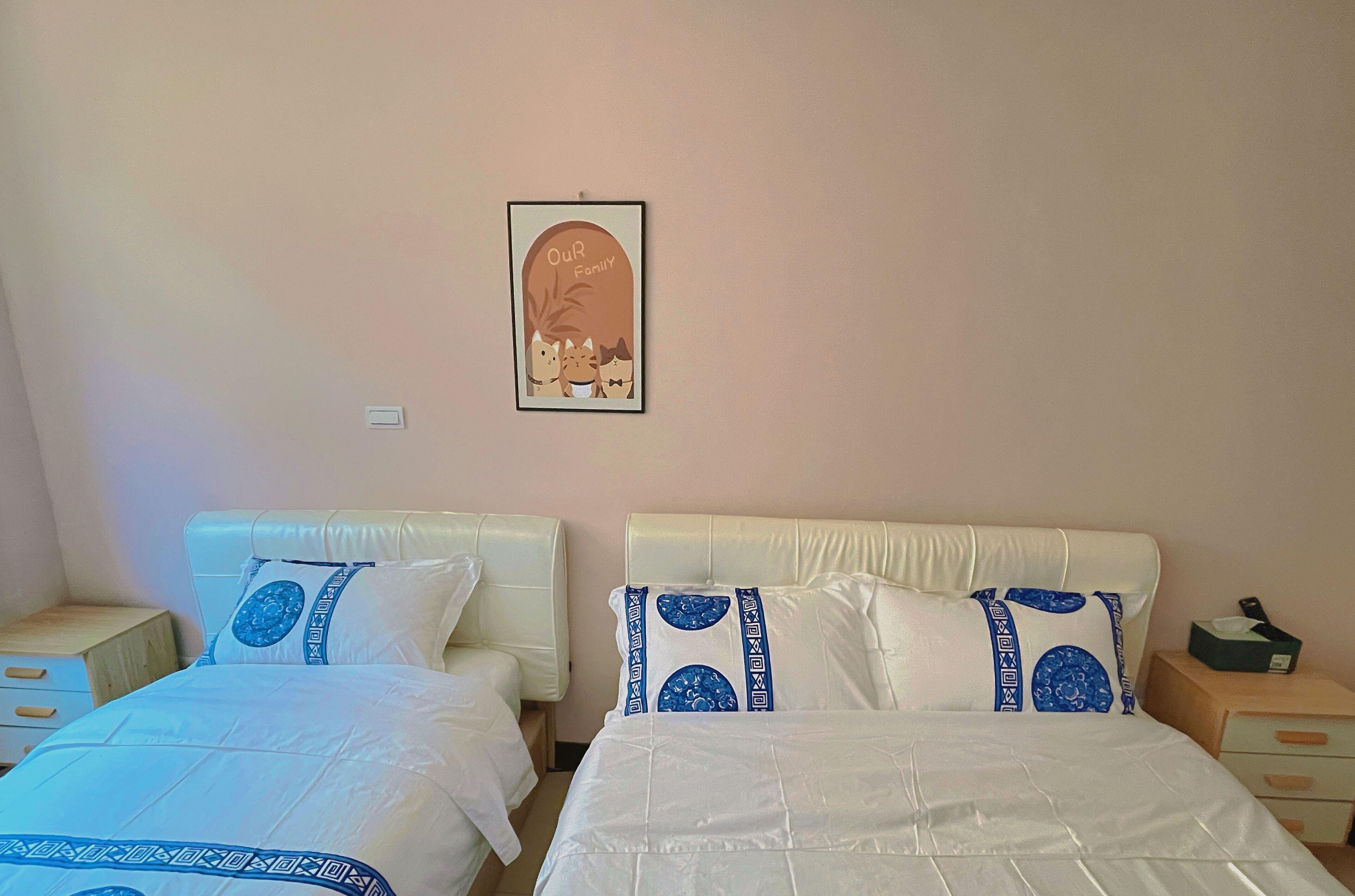 Une chambre d’hôtel avec deux lits, chacun agrémenté de draps blancs et d’oreillers décoratifs bleus, une œuvre d’art encadrée au mur et une table de chevet avec une boîte de mouchoirs.