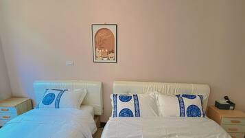 A hotel room with two beds, each with white bedding and blue decorative pillows, a framed artwork on the wall, and a bedside table with a tissue box.