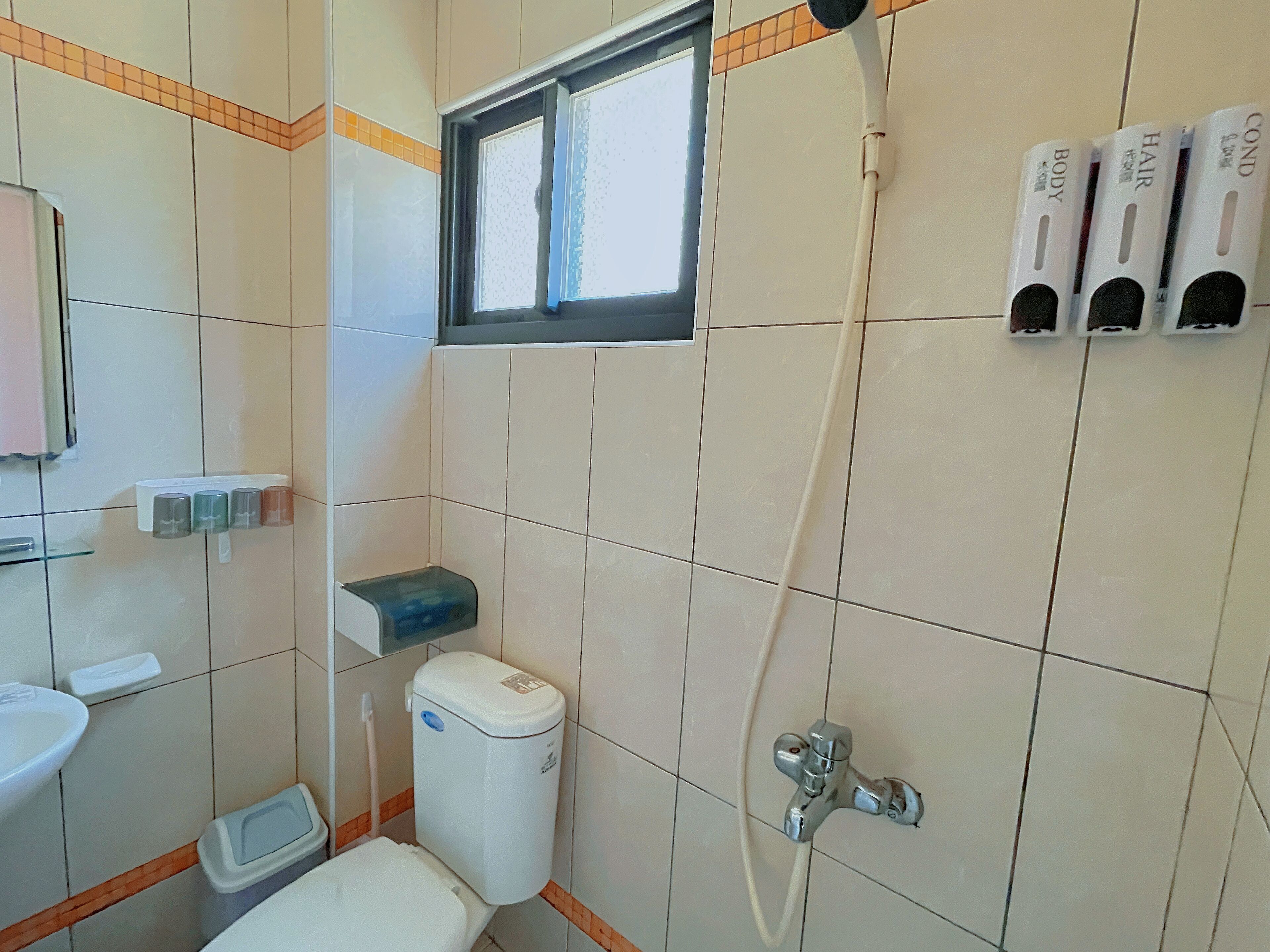 A small bathroom with a toilet, a sink, a window, and a shower.