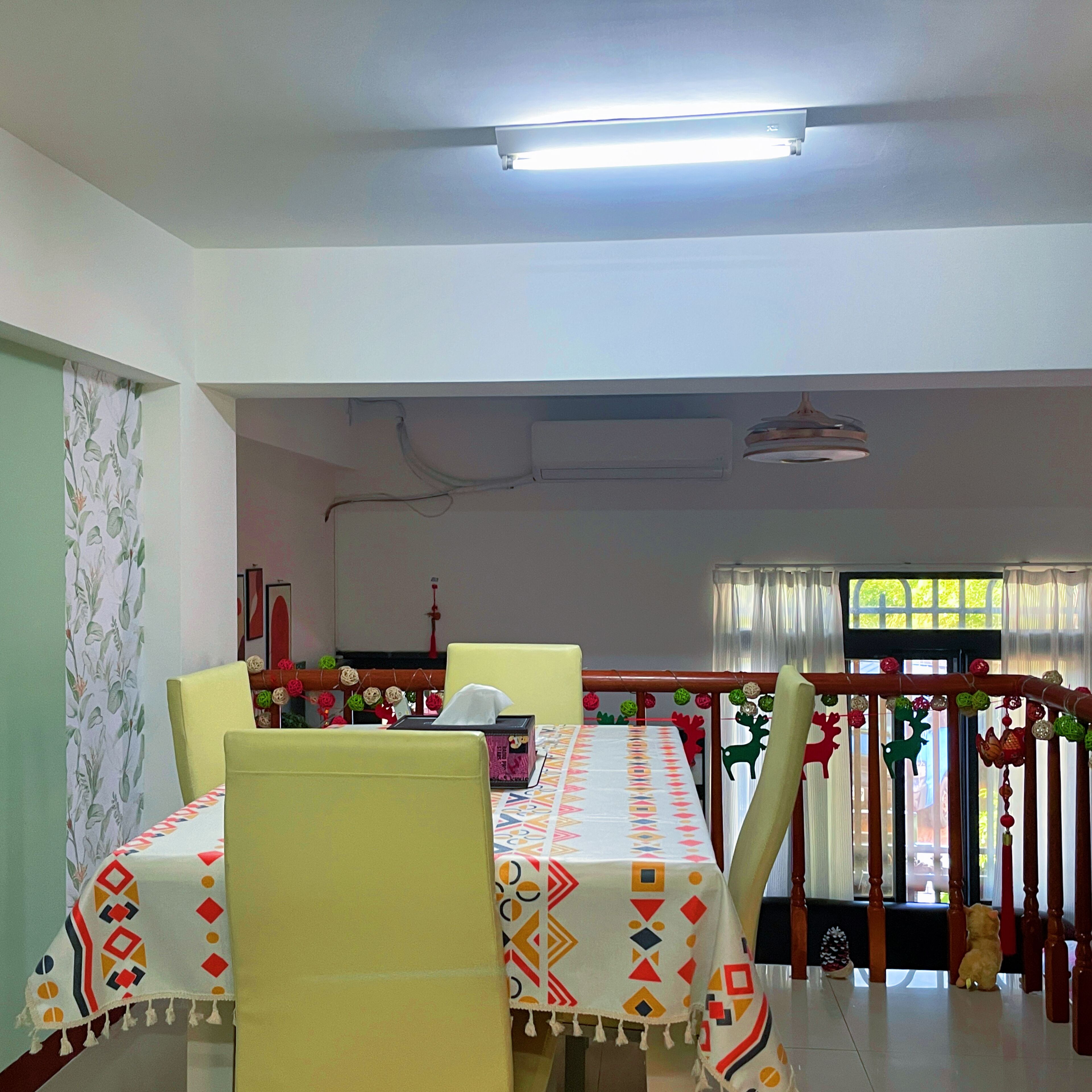 Un comedor con una mesa cubierta por un mantel estampado, sillas amarillas y una lámpara en el techo.