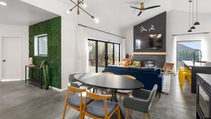 Una sala de estar moderna con un sofá azul, una mesa de comedor con sillas, una chimenea y una zona de cocina con taburetes amarillos.