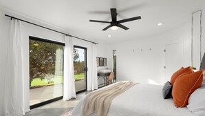 Un dormitorio moderno con una cama grande, un ventilador de techo y vistas a un jardín a través de una puerta corrediza de vidrio.