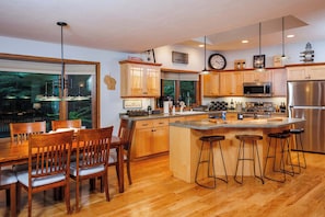 A modern kitchen with wooden cabinets, a stainless steel refrigerator, and a large island with bar stools.